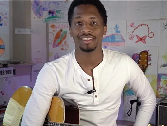 ron artis with his guitar and kids painting at the background