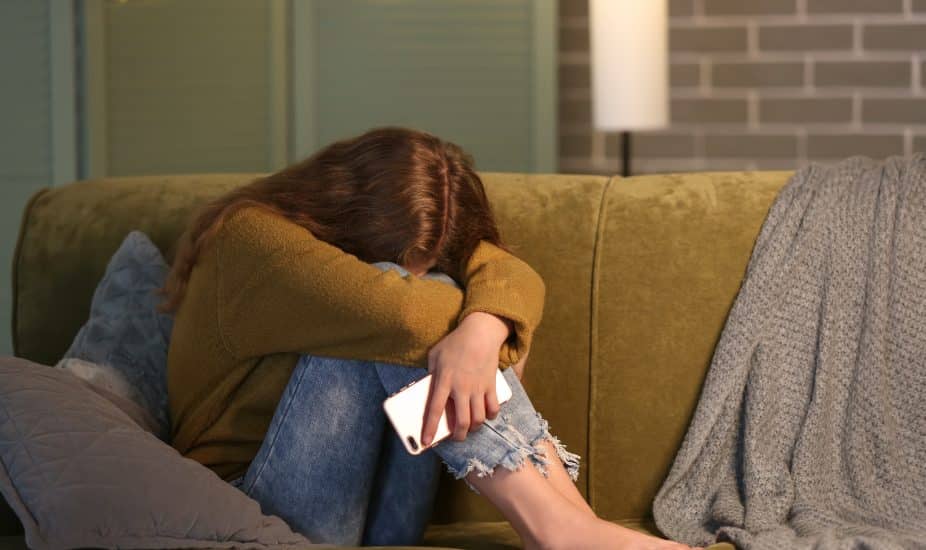 teenage girl with mobile phone on sofa at night