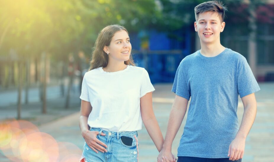 Two teenagers are walking in the sunlight and holding hands